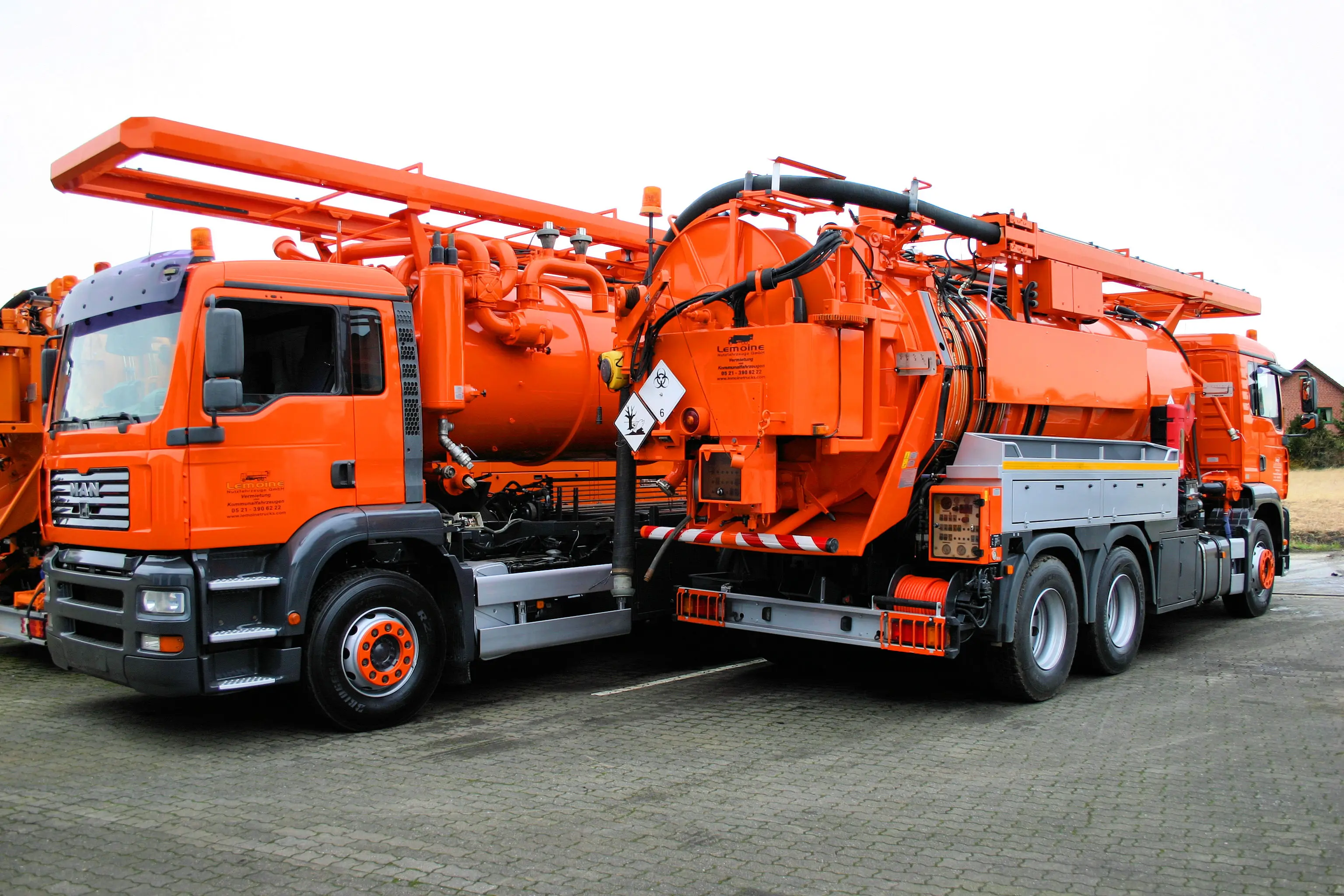 Nahaufnahme der Pumpen- und Schlauchtechnik am Tank eines orangen Saugwagens