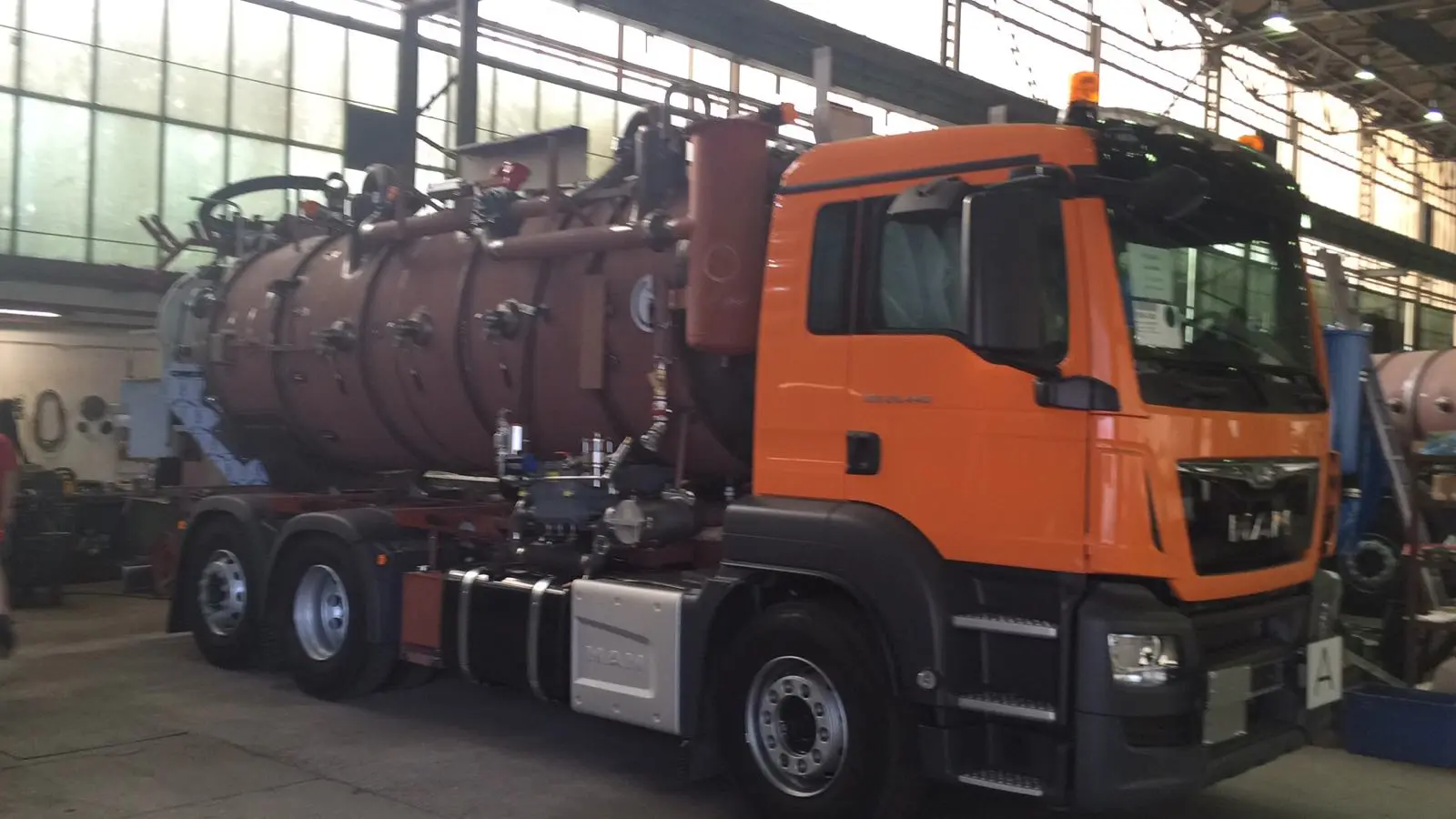Komplett montierter MAN-Saugwagen mit rotbraun beschichtetem Tank schräg von vorne in der Halle