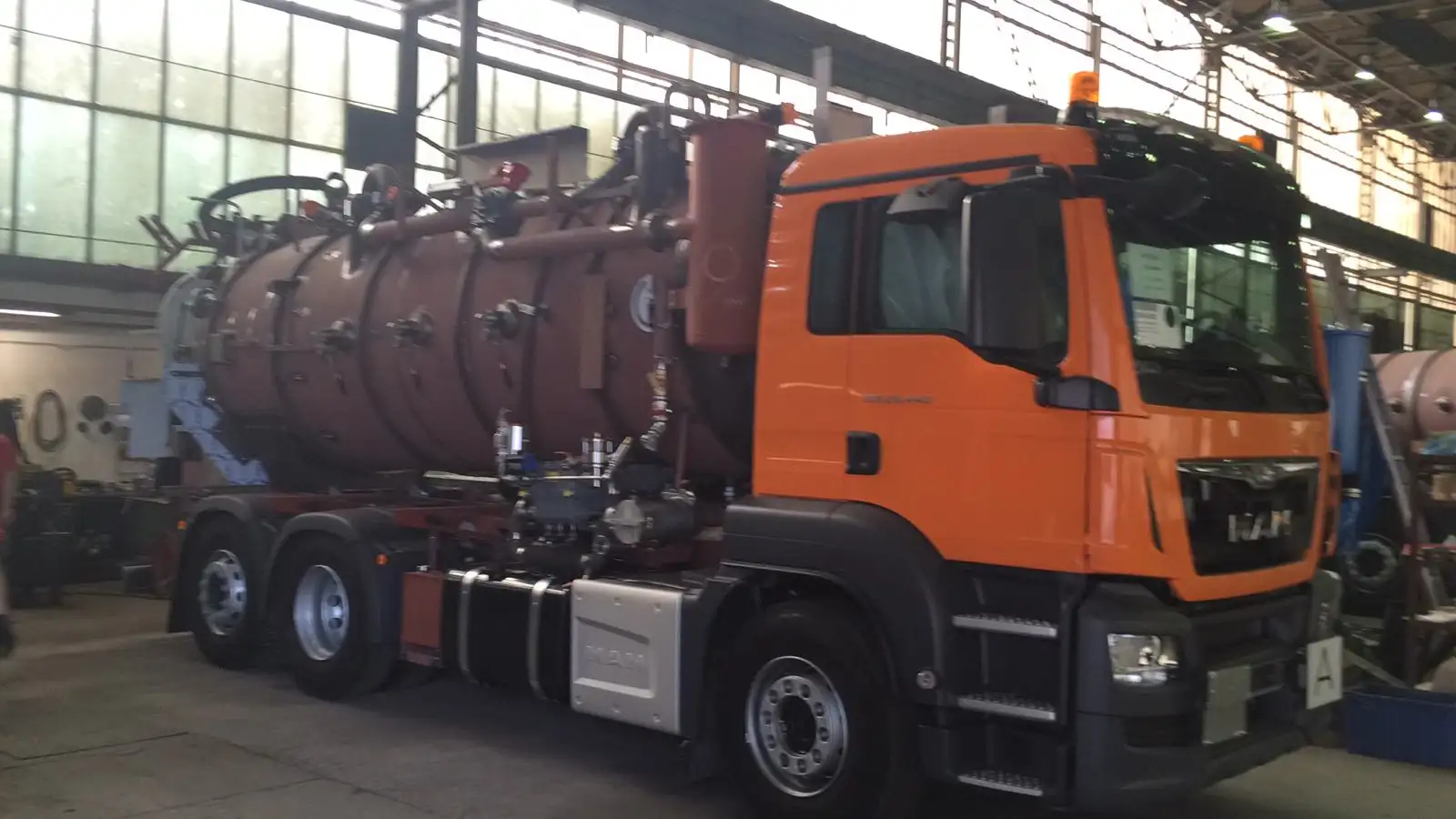 Komplett montierter MAN-Saugwagen mit rotbraun beschichtetem Tank schräg von vorne in der Halle